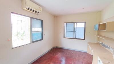 A well-lit bedroom with windows, wooden flooring, air conditioner, and built-in shelves.