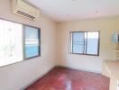 A well-lit bedroom with windows, wooden flooring, air conditioner, and built-in shelves.