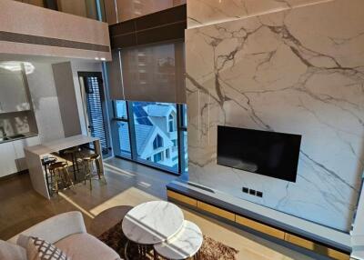 Modern living room with open-concept kitchen, marble accent wall, and large window