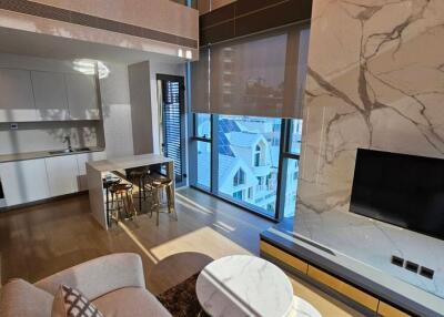 Modern open plan living room with kitchen featuring marble wall with TV, large windows, and island with bar stools