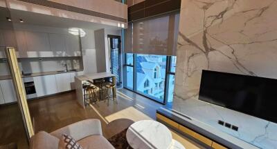 Modern open plan living room with kitchen featuring marble wall with TV, large windows, and island with bar stools