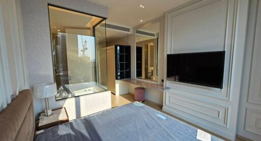 Bright and modern bedroom with a large window providing natural light, a wall-mounted TV, and an adjacent bathroom with a glass partition.