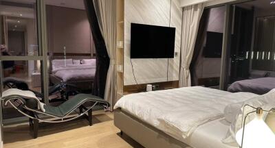 Modern bedroom with a large bed, chair, and wall-mounted TV