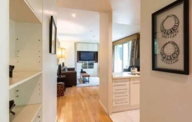 View of living room from hallway with wooden flooring, wall-mounted TV, and kitchen glimpse