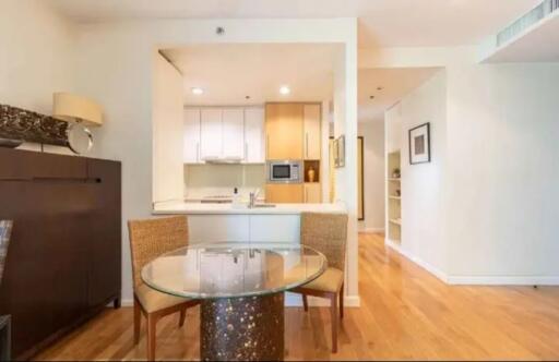 Modern dining area with glass table and wooden chairs next to kitchen