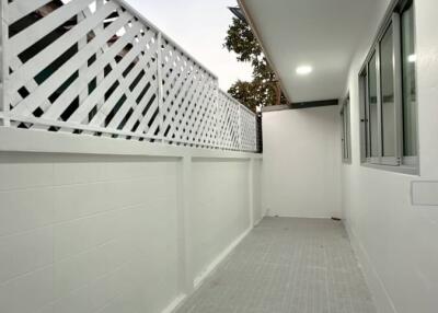 Narrow outdoor corridor with white walls, a lattice fence, and ceiling lights