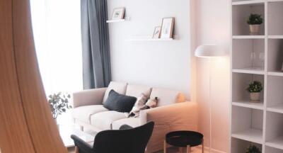 A cozy living room with modern decor, featuring a couch, a floor lamp, and wall-mounted shelves.