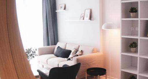 A cozy living room with modern decor, featuring a couch, a floor lamp, and wall-mounted shelves.