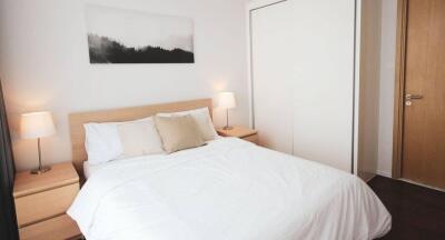 Modern bedroom with white bedding, wooden furnishings, and a minimalist design