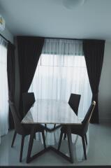 Modern dining area with a table and four chairs near large windows with curtains