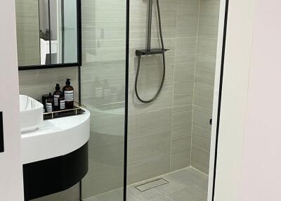 Modern bathroom with glass shower enclosure, rain showerhead, vanity sink, and toiletries.