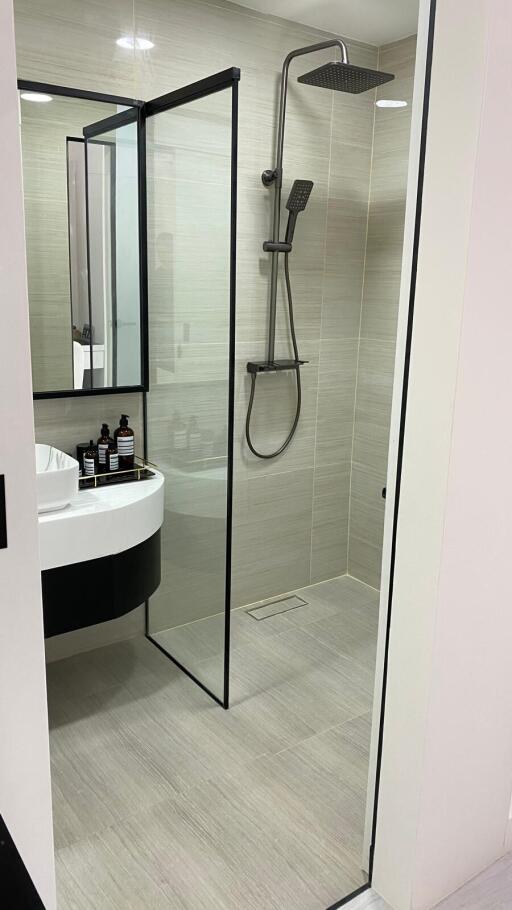 Modern bathroom with glass shower enclosure, rain showerhead, vanity sink, and toiletries.