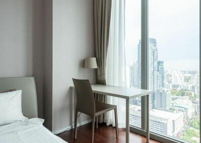 Bedroom with a city view through large windows, featuring a bed, a desk with a chair, and curtains