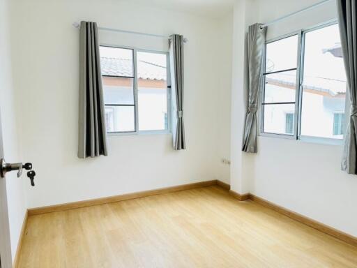 A bright bedroom with wooden flooring, two windows with grey curtains