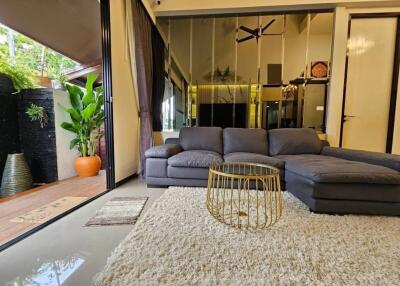 Modern living room with large sectional sofa, rug, and coffee table, adjacent to a patio with plants.