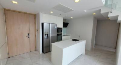 Modern kitchen area with wooden door, island counter, oven, refrigerator, and sleek design