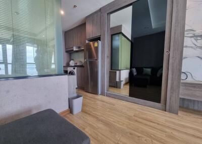Modern living area with an open kitchen featuring wood flooring, stainless steel refrigerator, and a glass partition