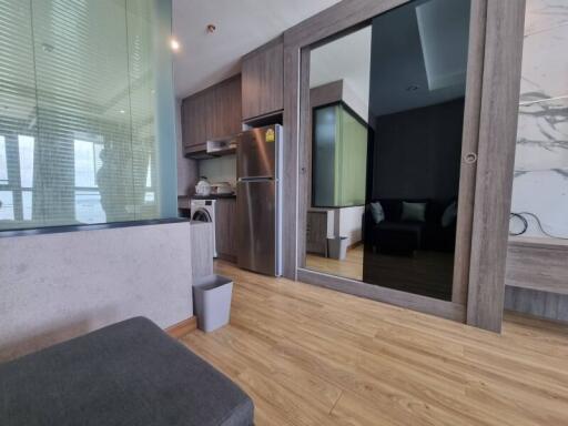 Modern living area with an open kitchen featuring wood flooring, stainless steel refrigerator, and a glass partition