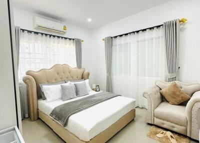 A well-lit bedroom with a large upholstered bed, armchair, bedside table, and neutral-colored decor