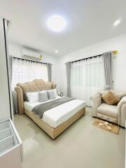 A well-lit bedroom with a large upholstered bed, armchair, bedside table, and neutral-colored decor