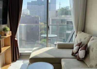 Living room with a view of the city, including a sofa, TV, shelves, and a glass door opening to a balcony.