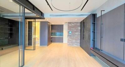 Modern living room with wooden flooring and glass partition, featuring an open view of the kitchen.