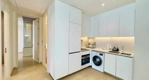 Modern kitchen with white cabinets, built-in appliances, and a washing machine.