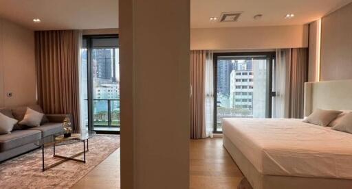 A photo of a modern bedroom adjoining a living area with large windows and city views