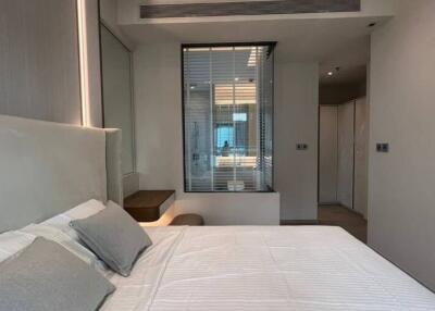 Modern bedroom with white bedding and wall-mounted shelf, featuring large mirror, windows, and built-in storage