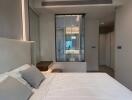 Modern bedroom with white bedding and wall-mounted shelf, featuring large mirror, windows, and built-in storage