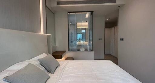 Modern bedroom with white bedding and wall-mounted shelf, featuring large mirror, windows, and built-in storage