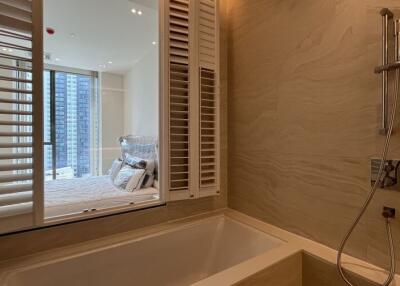 Modern bathroom with bathtub and shower, overlooking bedroom with bed and large window