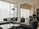 Modern living room with a large gray sectional sofa, a glass coffee table, and a nearby study area.