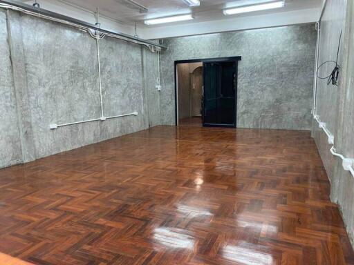 Spacious room with polished wooden flooring and concrete walls, featuring modern lighting fixtures