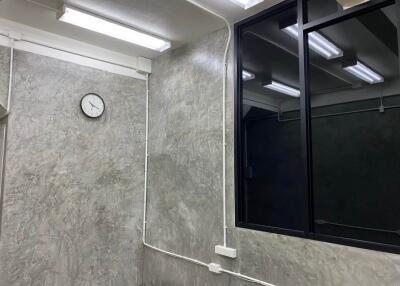 Room with grey textured walls, fluorescent lighting, a clock, and a large black-framed window