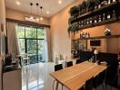 Modern dining area with a wooden table and chairs, shelves with plants and bottles, large window, and cozy ambiance