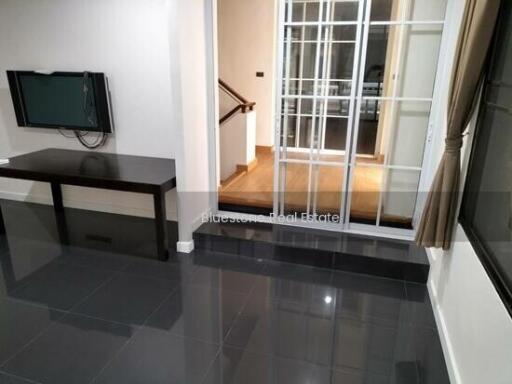 Modern living room with flat-screen TV and glass door opening to a hallway