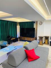 Modern living room with gray sofa, red pillow, large TV, and green curtains