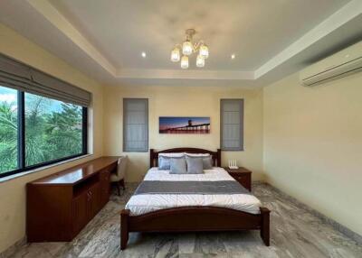 A spacious bedroom with a large bed, wooden furniture, a desk, a chair, and an air conditioner