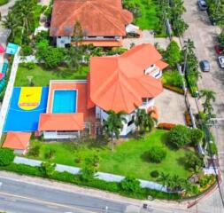 Aerial view of a large house with a red roof, swimming pool, and a colorful basketball court