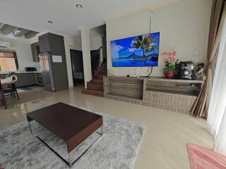 Spacious living room with modern decor, large flat screen TV, and access to kitchen and dining area