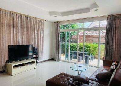 Spacious living room with a large TV, sectional sofa, glass coffee table, and sliding glass doors leading to an outdoor patio area