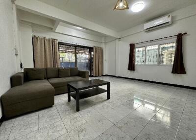 Spacious and well-lit living room with sofa, coffee table, large windows, and air conditioning unit