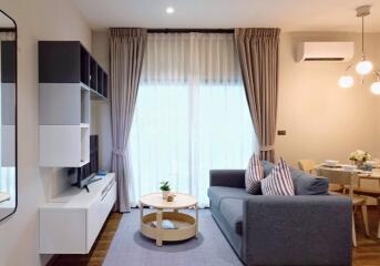 Modern living room with a gray sofa, wall-mounted TV, air conditioning, and dining area