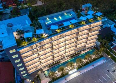 Aerial view of a modern apartment building with a rooftop pool and surrounding greenery