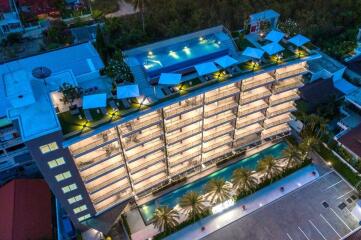 Aerial view of a modern apartment building with a rooftop pool and surrounding greenery