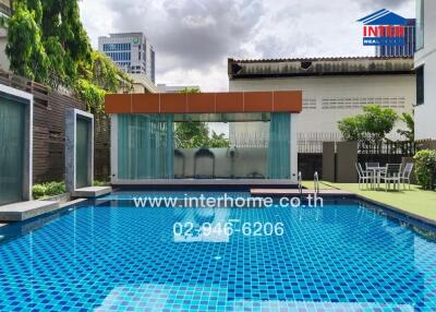 Outdoor swimming pool with blue tiles, surrounded by buildings and greenery