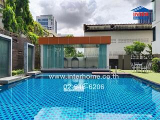 Outdoor swimming pool with blue tiles, surrounded by buildings and greenery