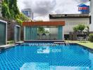 Outdoor swimming pool with blue tiles, surrounded by buildings and greenery