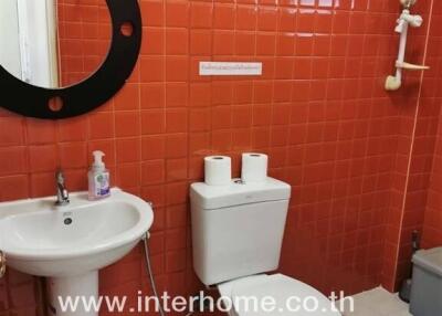 Bathroom with red tiled wall, round mirror, sink, and toilet